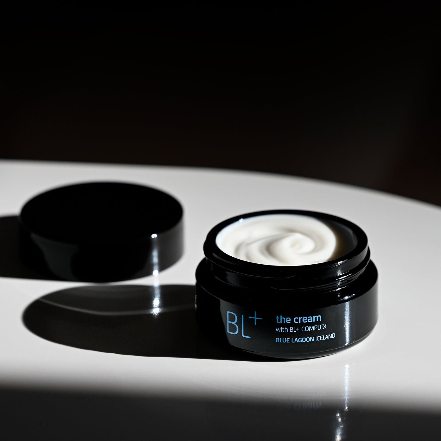 Open jar of BL+ The Cream on reflective surface with cream visible inside