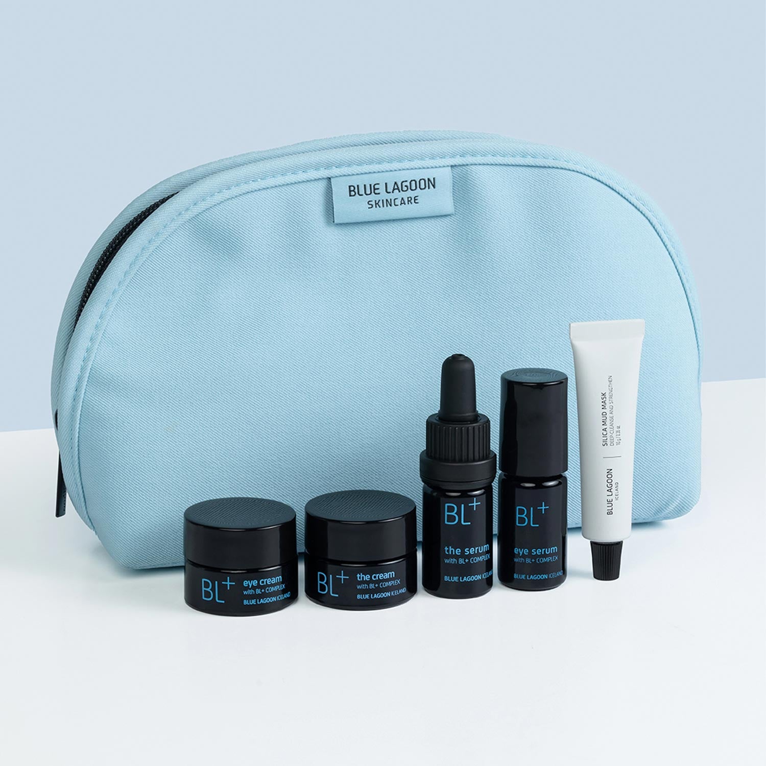 Blue Lagoon skincare products including jars, a dropper, and a tube in front of a blue pouch on a light gray background.