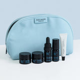 Blue Lagoon skincare products including jars, a dropper, and a tube in front of a blue pouch on a light gray background.