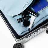 Open suitcase with cosmetic products and a passport on a light blue fabric