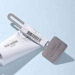 Tube/Mask Squeezer Key attached to aluminum skincare tube on light blue background